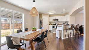 A modern kitchen with white cabinets, a wooden dining table, and black chairs. - 🌞 Meridian BNB - 4BR/2.5BA Huge Backyard: Near Eagle, Star, Boise, The Village (Meridian)