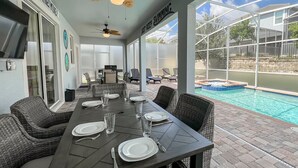 A covered patio with a dining table set for four, a pool, and a ceiling fan.