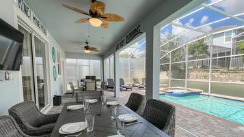 Un patio cubierto con una mesa de comedor para cuatro personas, una piscina y un ventilador de techo.