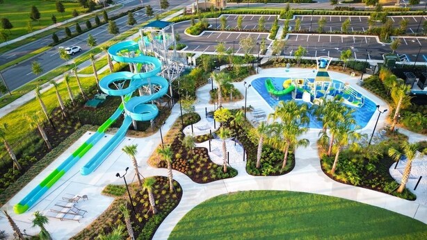 An aerial view of a water park with multiple slides and pools, surrounded by landscaped areas and palm trees.