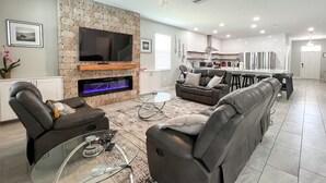 A modern living room with a stone fireplace, a flat-screen TV, and a glass coffee table.