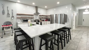 A modern kitchen with a large island, black bar stools, stainless steel appliances, and white subway tiles.