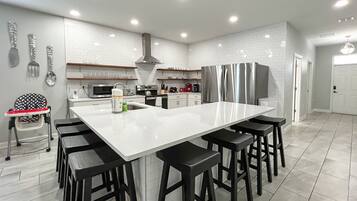 Una cocina moderna con una isla grande, taburetes negros, electrodomésticos de acero inoxidable y azulejos blancos tipo metro.