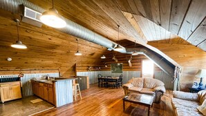 A spacious loft with wooden floors, a dining area, a kitchen with a bar, and a cozy seating area. - Quiet Crystal Creek Ranch Bunkhouse with large private pond (Brackettville)