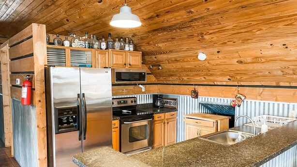 A compact kitchen with a stainless steel refrigerator, microwave, oven, and a granite countertop. - Quiet Crystal Creek Ranch Bunkhouse with large private pond (Brackettville)