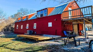 A red building with a large deck and a covered porch. - Quiet Crystal Creek Ranch Bunkhouse with large private pond (Brackettville)