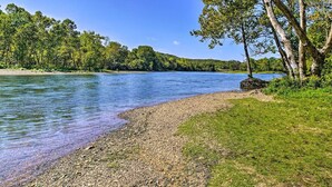 A riverbank with pebbles and grass, trees, and a clear blue sky. - Woodsy Wonder - Pools, Hot tub, Gated & Golf CENTRAL LOCATION (Branson)