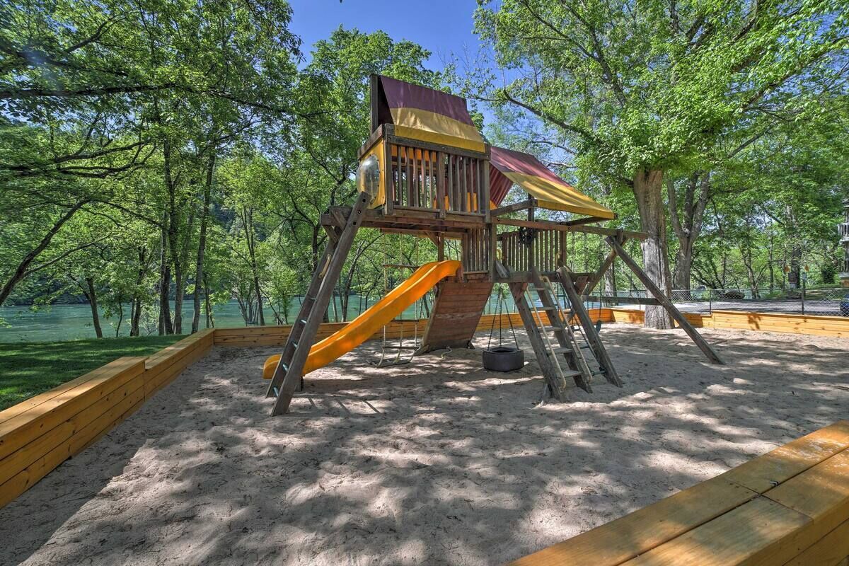 Une structure de jeux en bois, dotée d’un toboggan et d’une zone d’escalade, entourée de sable et d’arbres.