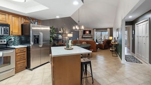 A modern kitchen with a central island, stainless steel appliances, wooden cabinets, and a dining area with a couch and chairs. - Woodsy Wonder - Pools, Hot tub, Gated & Golf CENTRAL LOCATION (Branson)