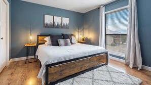 A bedroom with a bed, bedside lamps, a window with curtains, and a wall with three framed pictures. - Woodsy Wonder - Pools, Hot tub, Gated & Golf CENTRAL LOCATION (Branson)
