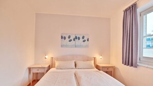 A double bed with two nightstands, a wall-mounted painting, and a window with curtains. - Hanseatic Residence Apartment 4 - Hanseatic Residence (Scharbeutz)
