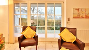 A room with two brown leather chairs with yellow cushions, a large sliding glass door to a garden, and a painting on the wall. - Hanseatic Residence Apartment 4 - Hanseatic Residence (Scharbeutz)