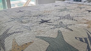 A bedroom with a bed featuring a starfish-patterned quilt, a view of the ocean through a window, and a white lamp on a bedside table. - Tranquility reigns at Talisman (Elbow Cay)