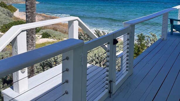 A wooden deck with white railings overlooking a beach with clear blue water and a palm tree. - Tranquility reigns at Talisman (Elbow Cay)
