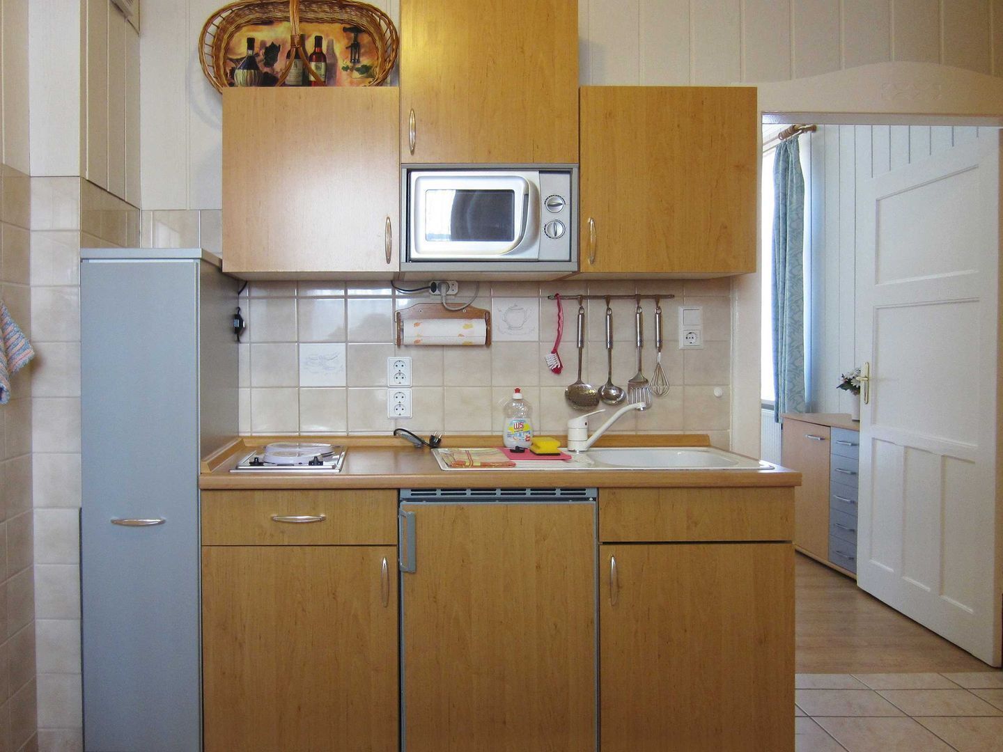 A compact kitchen with wooden cabinets, a built-in microwave, a sink, and a dish rack.