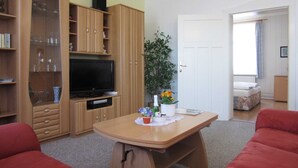 Una sala de estar con televisor, muebles de madera, una mesa de comedor con un florero y un sofá rojo.