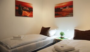 A hotel room with two beds, white bedding, a nightstand with a lamp, and two paintings on the wall. - Gartenblick - Willkommen in der Ferienwohnung Gartenblick in Kröpelin (Kröpelin)