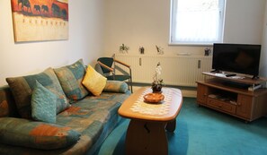 A living room with a sofa, a coffee table, a television, and a radiator. - Gartenblick - Willkommen in der Ferienwohnung Gartenblick in Kröpelin (Kröpelin)