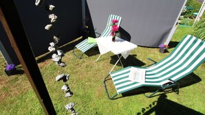 En patio med to loungestole med grønne striber og et lille bord, omgivet af et sort telt og dekorative sten.
