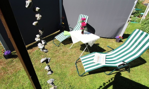 A patio area with two green-striped lounge chairs and a small table, surrounded by a black tent and decorative stones.