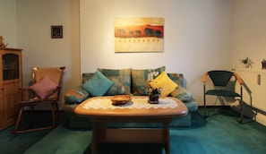 A cozy living room with a rocking chair, a sofa with colorful cushions, and a table with a decorative item.