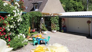 Een overdekt terras met een tafel en stoelen, omringd door potplanten en bloemen.