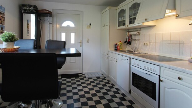 Een keuken met witte kasten, een zwart-wit geruit vloertje, een eettafel met stoelen en een fornuis.