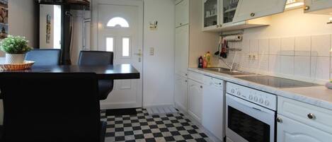 Een keuken met witte kasten, een zwart-wit geruit vloertje, een eettafel met stoelen en een fornuis.