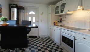 A kitchen with white cabinets, a black and white checkered floor, a dining table with chairs, and a stove. - Gartenblick - Willkommen in der Ferienwohnung Gartenblick in Kröpelin (Kröpelin)