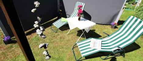 Eine Terrassenfläche mit zwei grün gestreiften Liegestühlen und einem kleinen Tisch, umgeben von einem schwarzen Zelt und dekorativen Steinen.