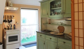 A kitchen with a stove, oven, and green cabinets. There is a window with a view of a deck and chairs outside.