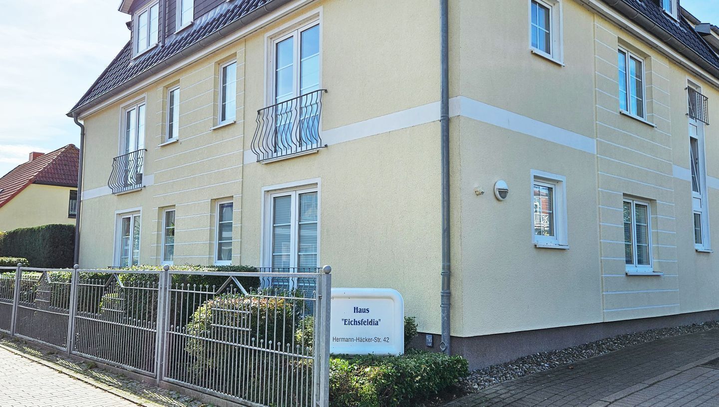 A multi-story residential building with a beige facade, balconies with metal railings, and a sign indicating the address "Hermann-Hacker-Str. 42".