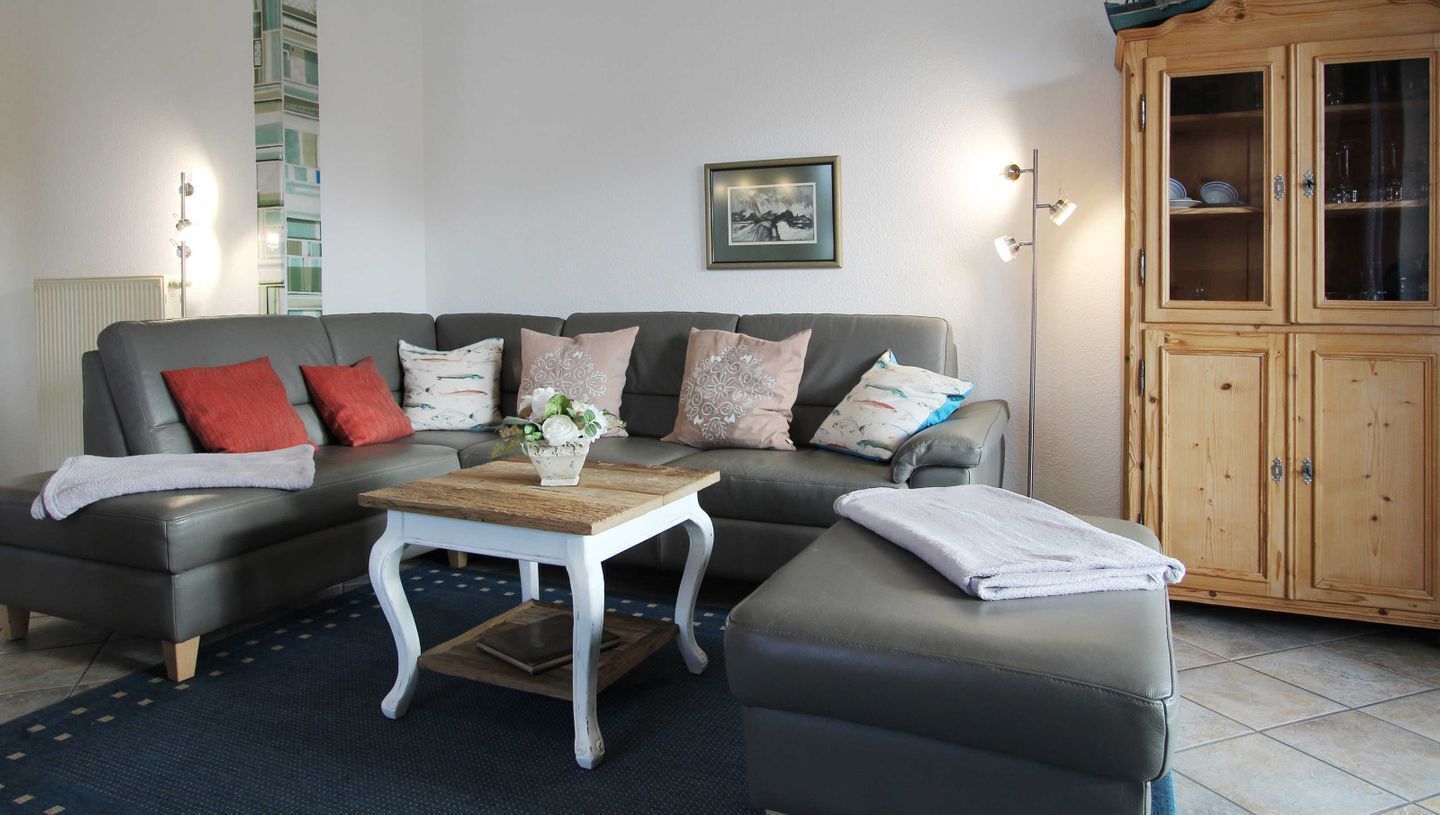 Een woonkamer met een grijze bank, een houten salontafel en een kast met glazen deuren.
