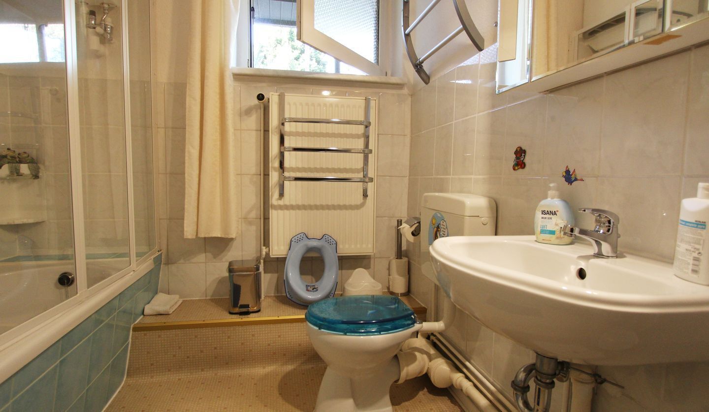 Un bagno con una vasca, un water con lo scudo azzurro, un lavandino bianco e una finestra.