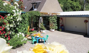 A covered patio area with a table and chairs, surrounded by potted plants and flowers.