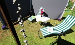 Un patio con dos sillones reclinables de rayas verdes y una mesita, rodeado por una carpa negra y piedras decorativas.