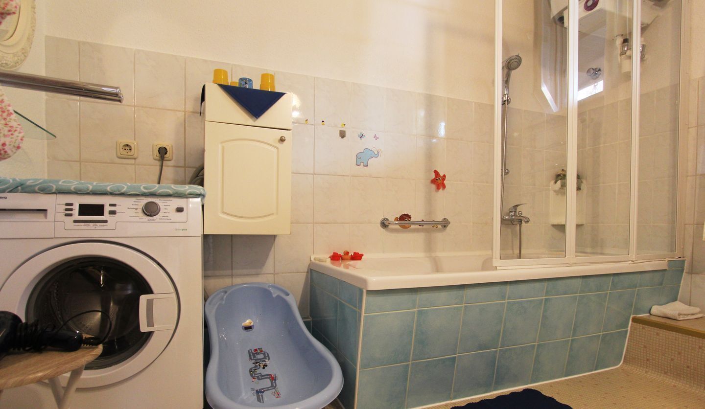 A bathroom with a washing machine, a blue bathtub, and a shower.