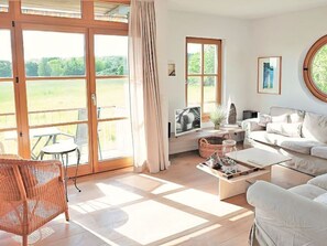 A spacious living room with a large sliding glass door, a white sofa, a wicker chair, and a coffee table.