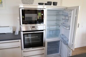 Eine kompakte Küche mit Einbauofen, Mikrowelle und Kühlschrank mit mehreren Fächern.