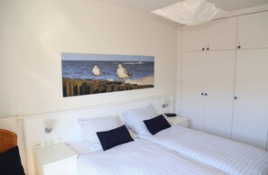 A bedroom with a bed, two pillows, a nightstand, a wall-mounted painting of seagulls, and a wardrobe.