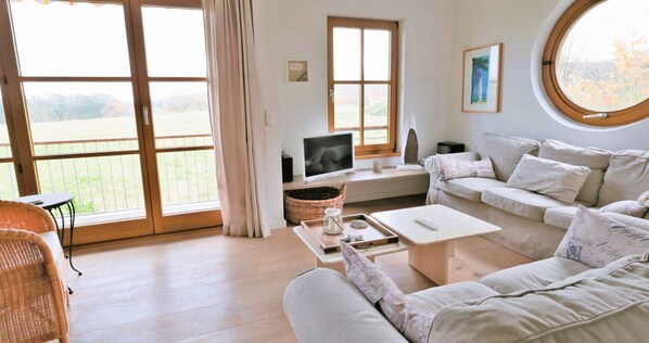 A spacious living room with a large window, a television, a sofa, and a dining table.