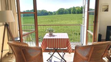 A balcony with wicker chairs, a table with a striped tablecloth, and a view of a green field.