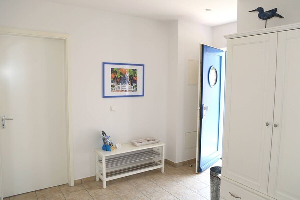 A hallway with a white door, a framed picture on the wall, a small white bench with magazines, and a blue door with a circular window.