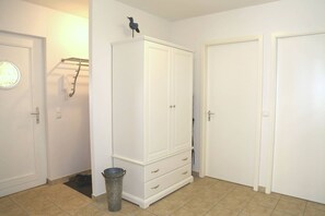 A hallway with a white wardrobe, a trash can, and a door with a towel rack.