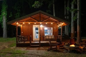 A cabin with a porch, outdoor seating, a fire pit, and a visible kitchen area.