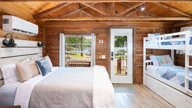 Une chambre de style cabane avec un plafond en bois, un lit avec une tête de lit, un lit superposé et une porte-fenêtre coulissante donnant sur un espace extérieur.