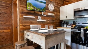 Une cuisine de style rustique, avec des éléments en bois, comprenant une table à manger, une horloge, un téléviseur et des appareils électroménagers modernes.