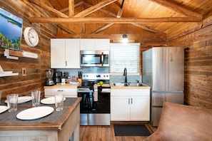 A compact kitchen with white cabinets, a microwave, a stove, and a refrigerator. - Cabin 5 Waterfront Cedar Cabin, Deck (Hemphill)