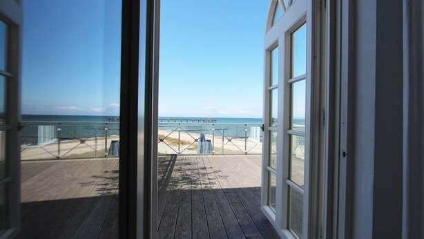 Una terraza de madera que conduce a una playa, con una vista despejada del océano y una barandilla de metal.