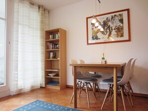 Un comedor con una mesa de madera, cuatro sillas, una estantería y una obra de arte enmarcada en la pared.